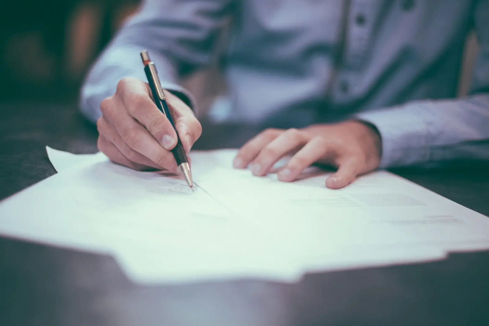 A hand signing a document with a fountain pen